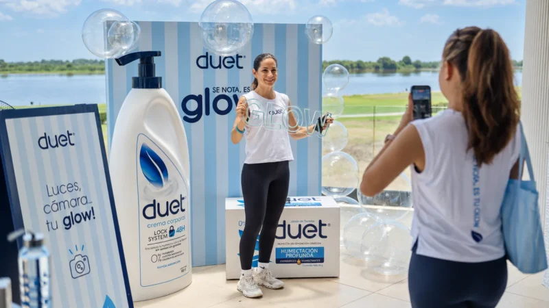 Persona posa con un letrero «Glow» en un photocall de la marca Duet mientras otra le toma una foto con el teléfono